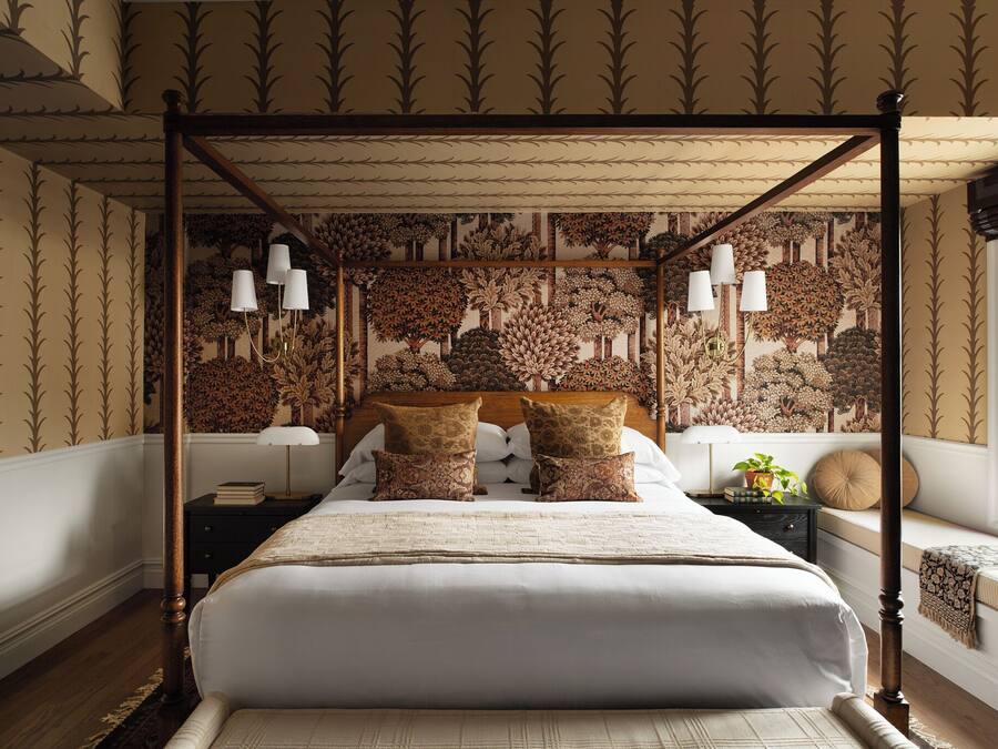 Ein Himmelsbett mit gemustertem Wandpapier, Nachttische und ein Fenster mit Blick.
