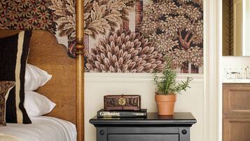Un dormitorio con cama con dosel, una mesita de noche con cajones, una planta en maceta y un tapiz de pared.