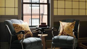 Two armchairs with patterned cushions, a small round table with a book, and a window with a view of a brick building.