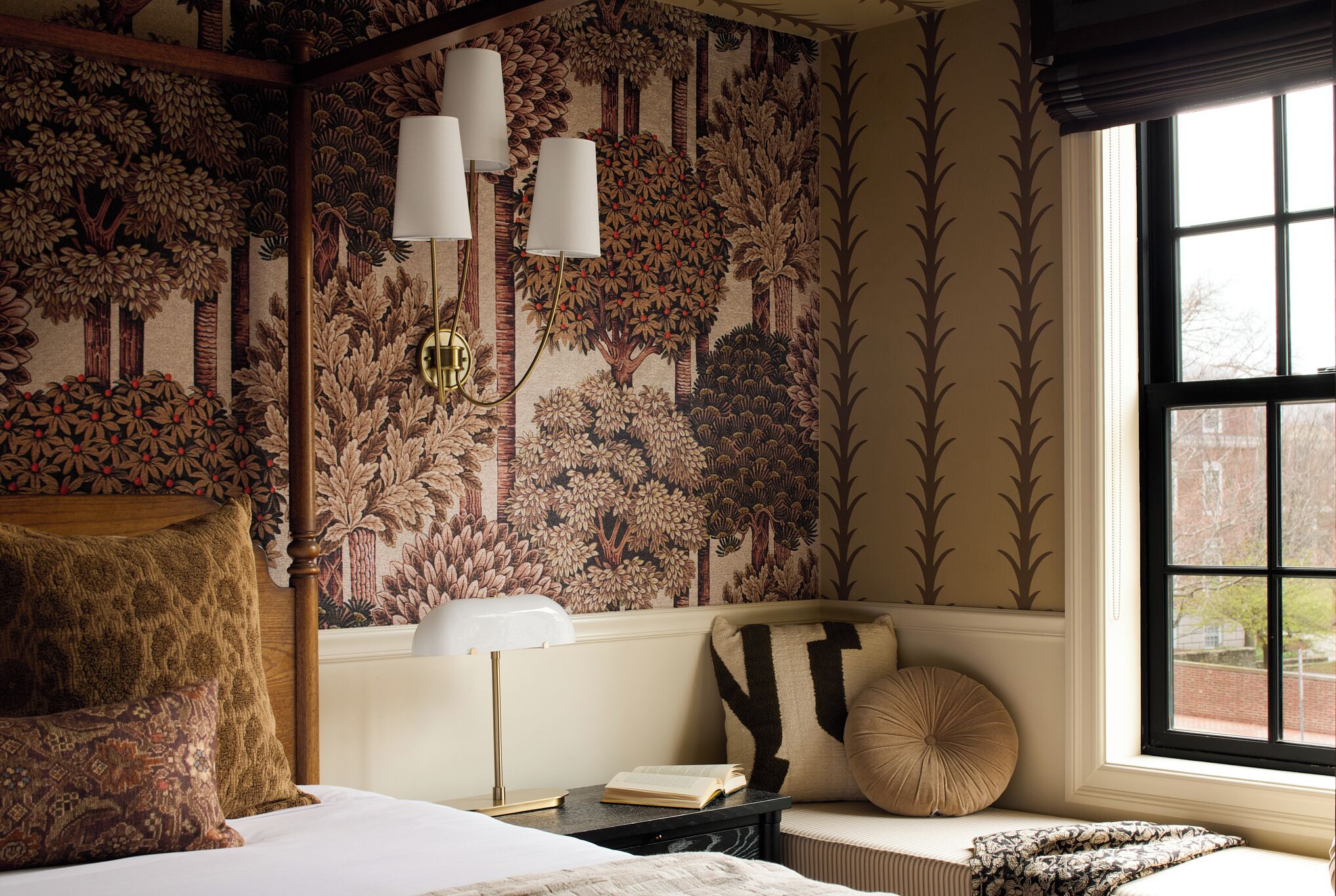 Une chambre avec un grand lit, une table de chevet, une lampe, une fenêtre donnant sur un beau paysage et un mur recouvert d’un papier peint à motifs naturels.