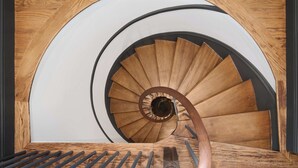 A spiral staircase with wooden steps and a metal handrail, enclosed by a wooden frame and white walls. - Cambridge Common House (Cambridge)