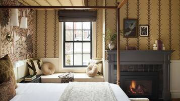 A bedroom with a four-poster bed, a fireplace, a window with blinds, and a bookshelf.