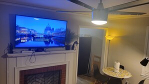 Un soggiorno con una televisione montata sulla mensola del camino, una ventola a soffitto, un tavolo da pranzo con sedie e una lampada.