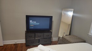 Camera d'albergo con televisore che mostra un canale sportivo, un letto con copriletto bianco, un piccolo comodino, uno specchio e una sedia in vimini.