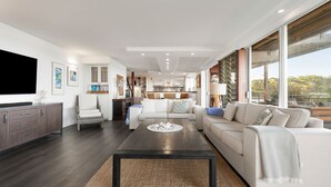 A spacious living room with a large flat-screen TV, a dark wooden coffee table, and a comfortable sofa set.