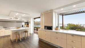 A modern kitchen with a large island, wooden flooring, and a view of the sea.