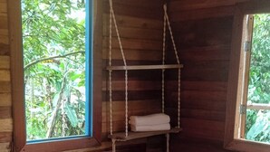 A wooden cabin room with a bed, a hanging chair, and a window with a view of greenery. - Cabin in the Salento cloud forest (Salento)