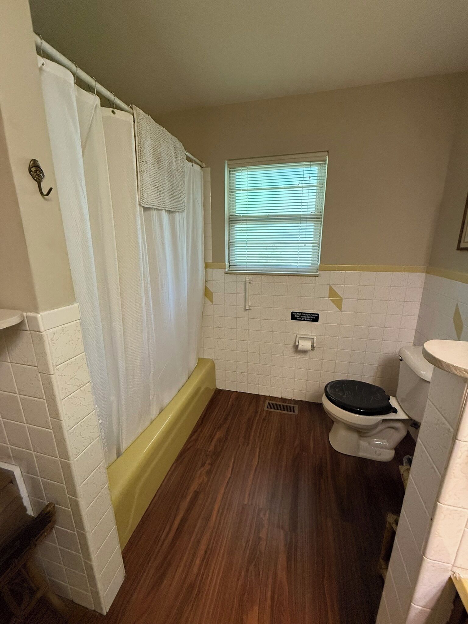 A small bathroom with a toilet, a shower curtain, a window with blinds, and a tiled wall.