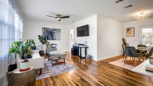 Ein modernes Wohnzimmer mit Holzboden, Deckenventilator, Flachbildfernseher und Essbereich mit Tisch und Stühlen.