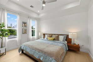 A bedroom with a large bed, two bedside lamps, a nightstand, a ceiling fan, and a window with curtains. - Amalfi Suite in Montrose (Houston)