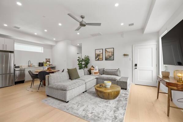 A modern living room with a grey sectional sofa, a wooden coffee table, and a dining area with a table and chairs. - Amalfi Suite in Montrose (Houston)