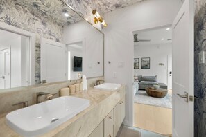 A modern bathroom with two sinks, a large mirror, and a vanity with storage. - Amalfi Suite in Montrose (Houston)