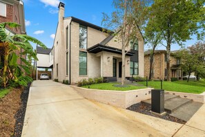 A modern two-story house with a concrete driveway, a well-maintained lawn, and a large tree in the front yard. - Amalfi Suite in Montrose (Houston)