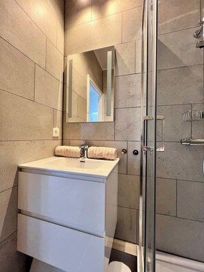 Une salle de bain moderne avec une douche à parois de verre, un grand miroir et un meuble-lavabo blanc agrémenté d’une serviette.