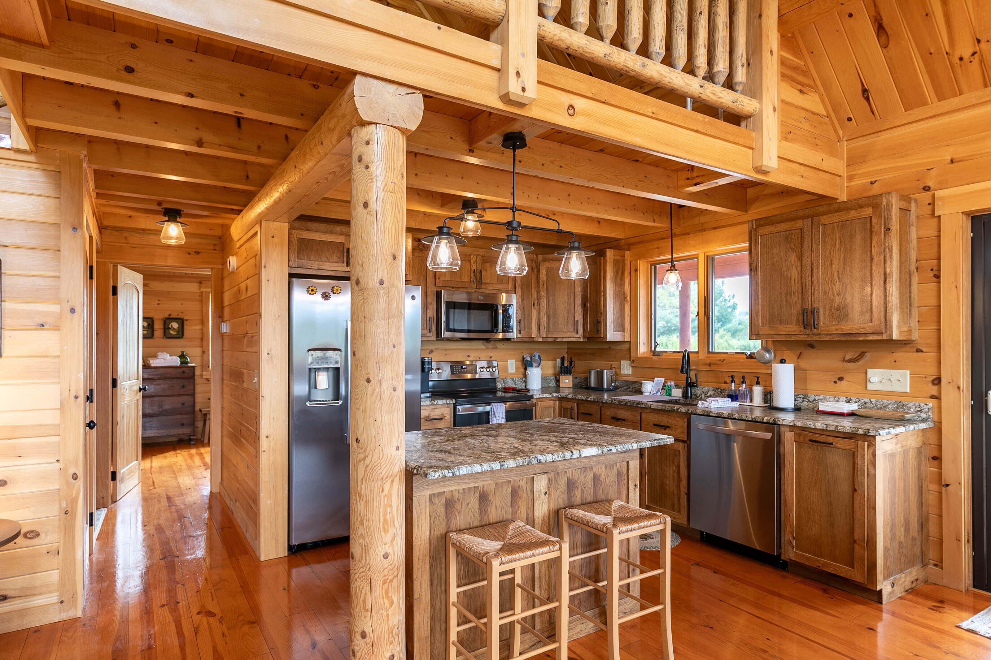 A wooden cabin interior with a kitchen, wooden floors, and a bar area with stools.