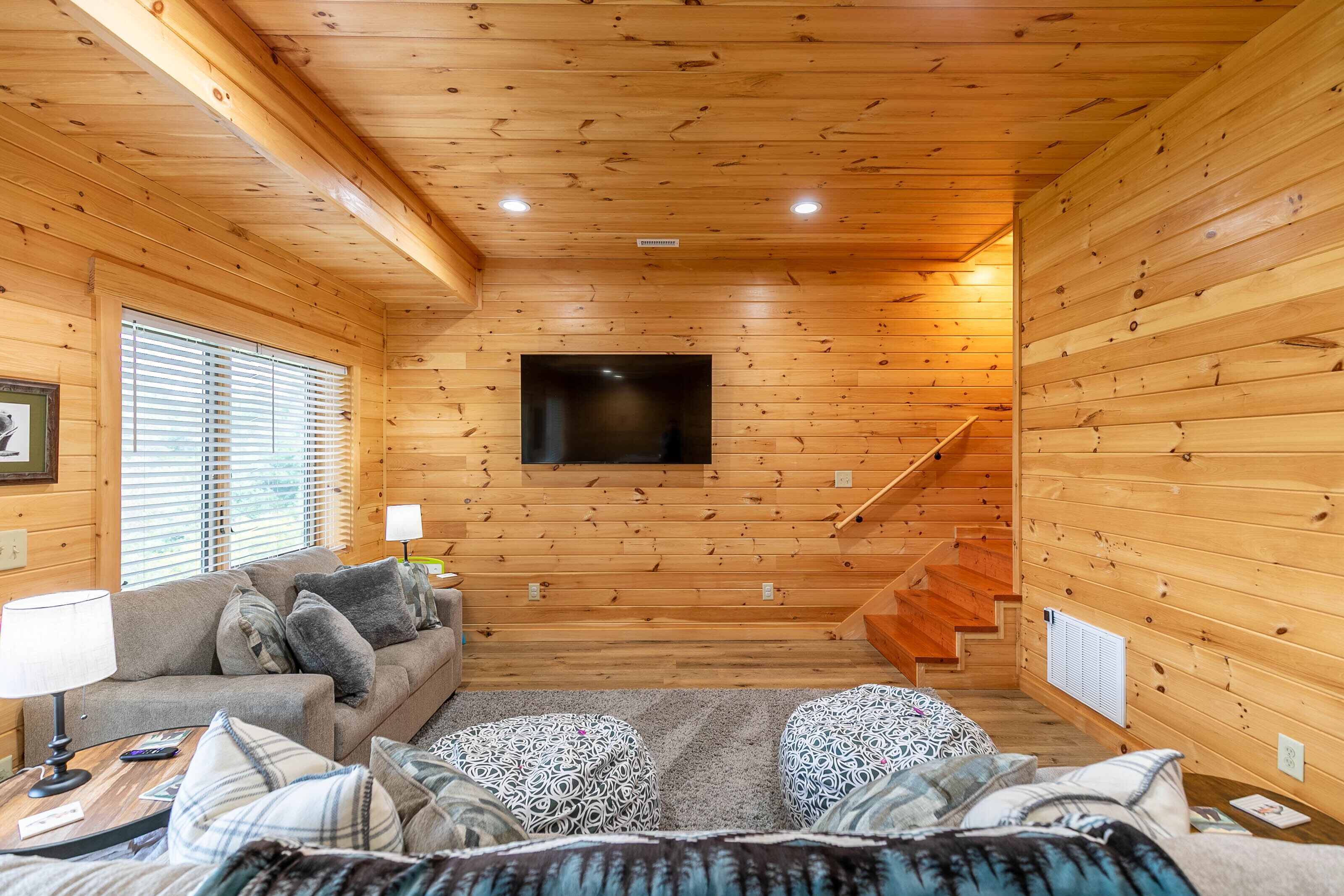 L’intérieur d’un chalet en bois chaleureux et accueillant, avec un canapé, des poufs, un téléviseur à écran plat et un escalier.