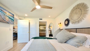 Un dormitorio con cama, ventilador de techo, una decoración grande en la pared y vistas al baño.