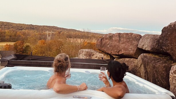 Twee personen in een jacuzzi met uitzicht op een glooiend landschap.