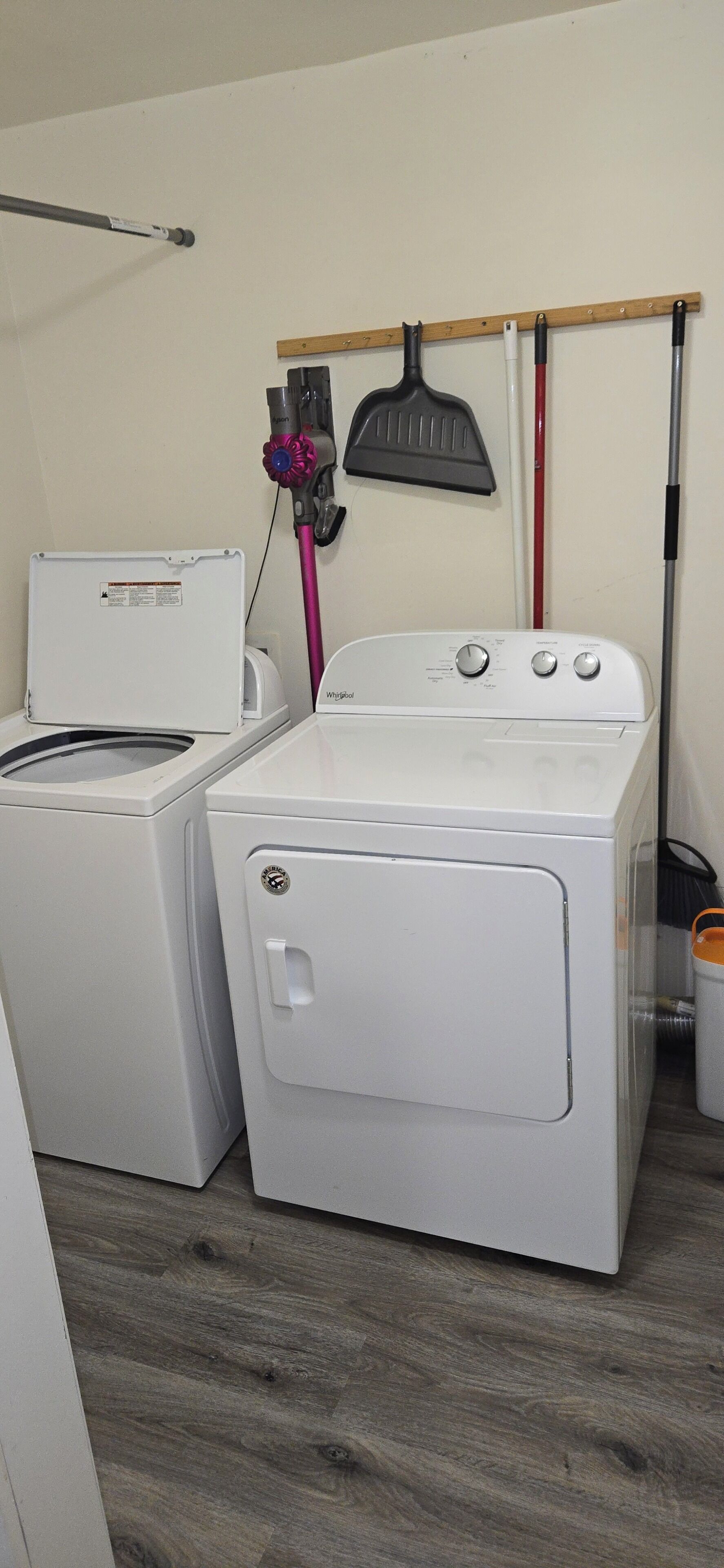 Een wasruimte met een voorlader wasmachine en droger, een bezem en een moprek.