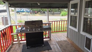 Un espacio al aire libre cubierto con una parrilla, un taburete de madera y vista a una calle con vehículos estacionados.