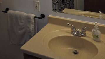 A bathroom with a beige sink, a mirror with lights, a towel rack, and a patterned curtain.
