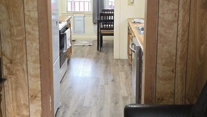 Un salón con un sofá de cuero negro, paneles de madera y vistas a una cocina y comedor.