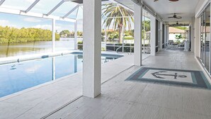 A covered outdoor area with a pool, palm trees, and a view of a lake. - Waterfront luxury estate. (Punta Gorda)