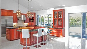 A modern kitchen with a large island, red cabinetry, and pendant lighting. - Waterfront luxury estate. (Punta Gorda)