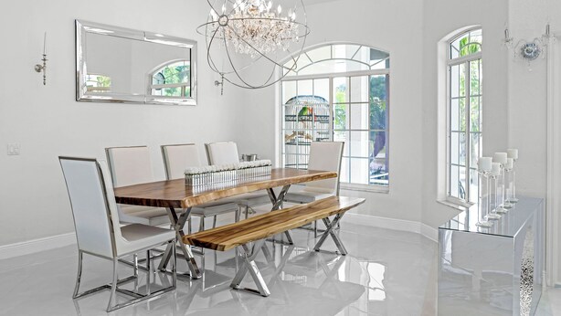A dining room with a wooden table, white chairs, a bench, and a chandelier. - Waterfront luxury estate. (Punta Gorda)
