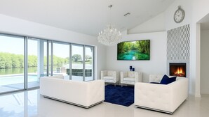 A modern living room with a large glass door leading to a pool, a fireplace, and a chandelier. - Waterfront luxury estate. (Punta Gorda)