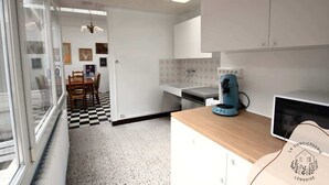 Una cocina moderna con armarios blancos, encimera de madera, una cafetera y una zona de comedor con suelo a cuadros.