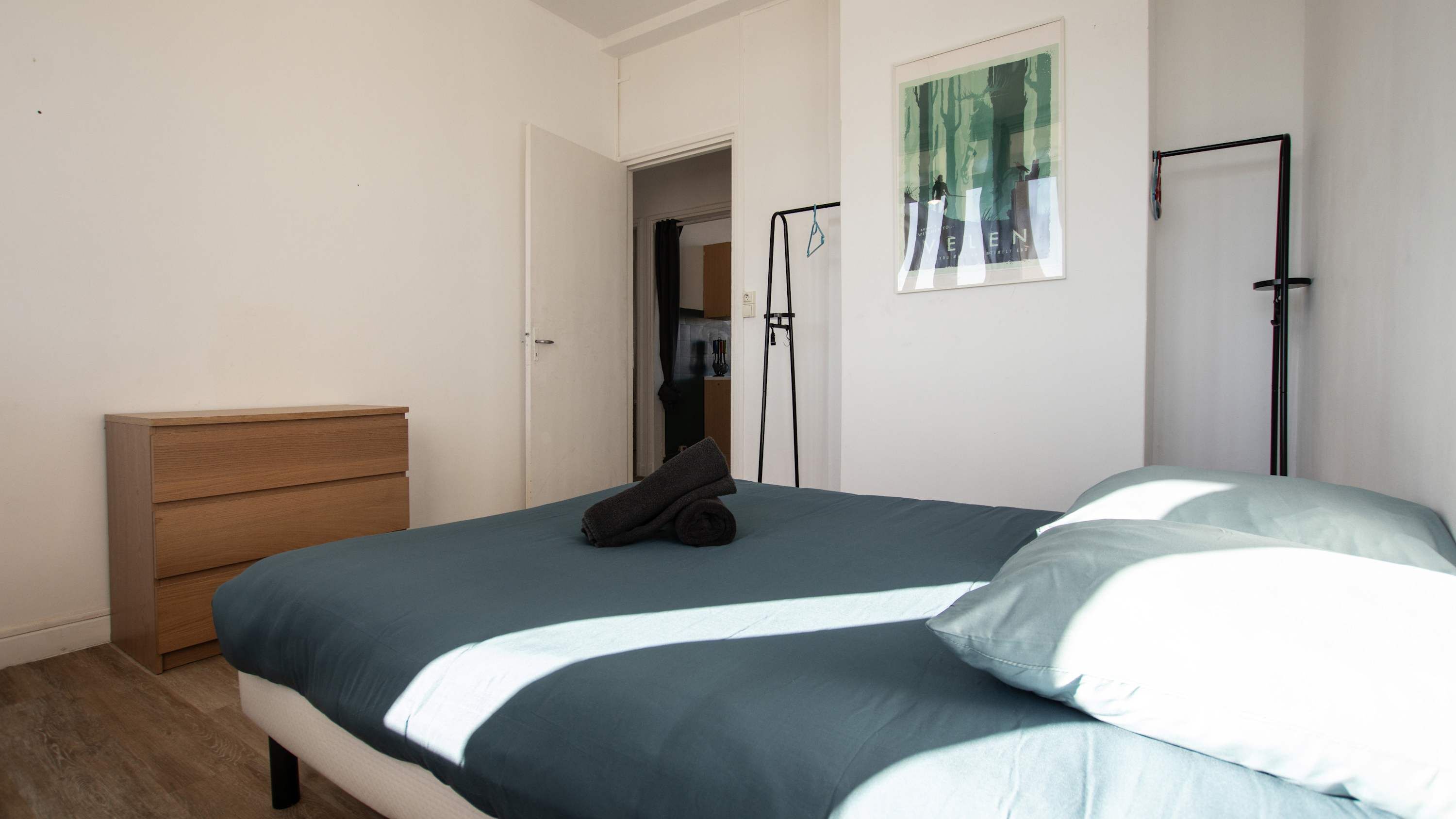 A bedroom with a bed, a wooden dresser, a door, and a poster on the wall.