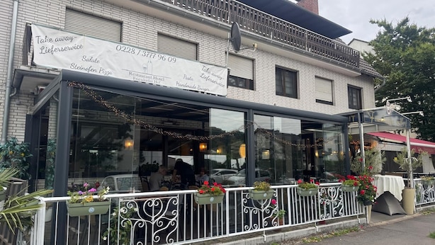A restaurant with a glass enclosure, outdoor seating with white railings, and flower planters. - Restaurant Hotel Friesdorfer Hof (Bonn)