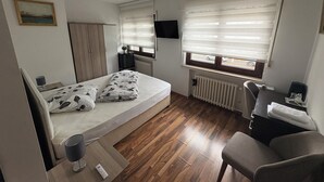 A bedroom with a bed, a desk, a chair, a radiator, a television, and a window with blinds. - Restaurant Hotel Friesdorfer Hof (Bonn)