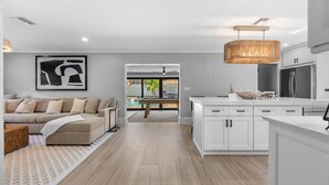A modern kitchen with white cabinetry, a central island, and a dining area with a view of the outdoors.