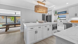 A modern kitchen with white cabinetry, a marble countertop, and a hanging light fixture.