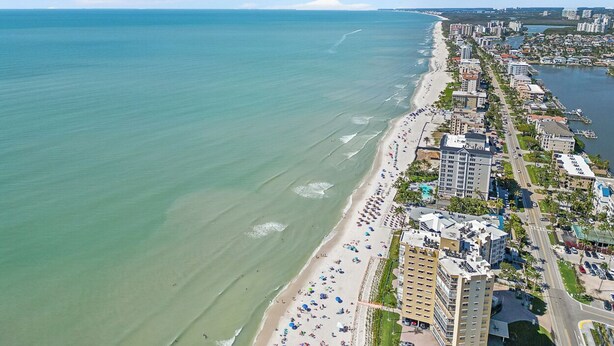 An aerial view of a coastal city with a long beachfront, high-rise buildings, and a clear sky.