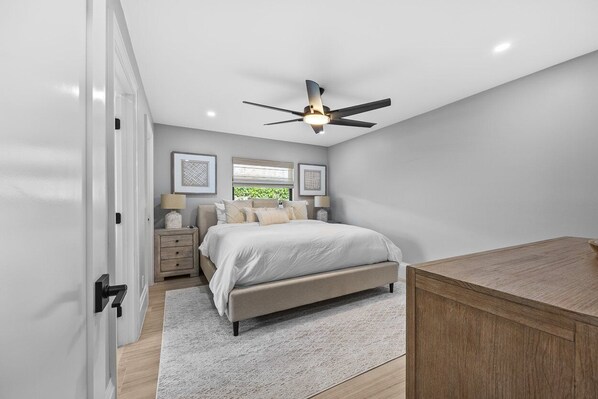 A bedroom with a bed, bedside tables, a ceiling fan, and a wooden dresser.
