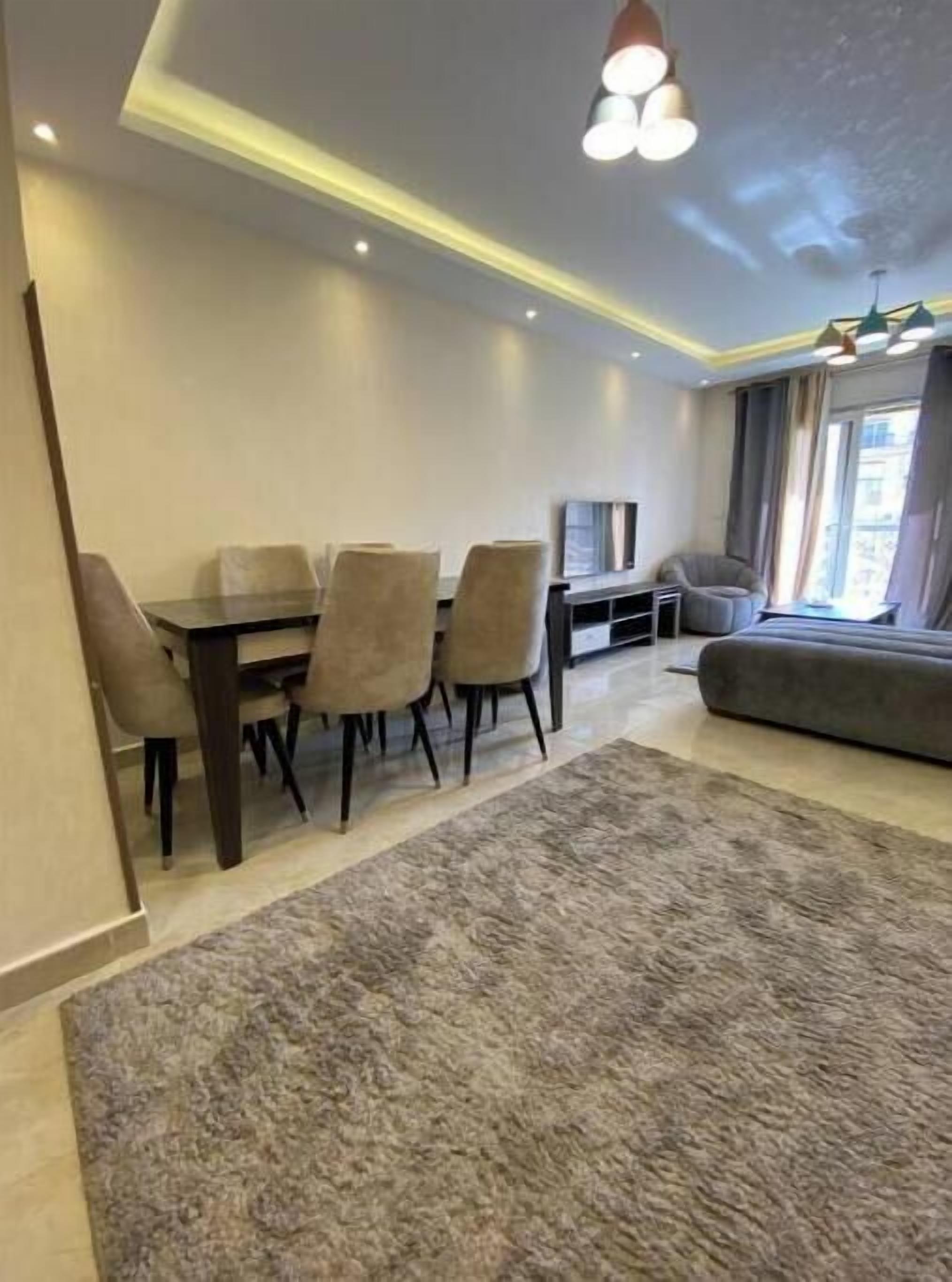 Un salon moderne avec un coin repas, un canapé gris et un téléviseur.