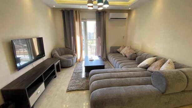 A modern living room with a sectional sofa, a flat-screen TV, a dark wooden entertainment unit, and a ceiling light fixture. - Alrehab and awesome (Cairo Governorate)