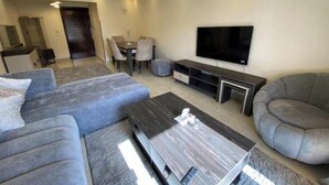 A modern living room with a grey sofa, a coffee table, a TV, and a dining area with chairs and a table. - Alrehab and awesome (Cairo Governorate)