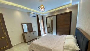 A modern bedroom with a large bed, a dresser, a mirror, and a wardrobe. - Alrehab and awesome (Cairo Governorate)