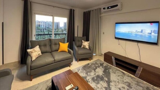 A modern living room with a grey sofa, a smaller armchair, a coffee table, and a flat-screen TV mounted on the wall. - Alrehab cozy apartment (Cairo Governorate)