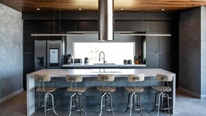 Une cuisine moderne dotée d’un îlot central, de tabourets de bar et d’une hotte de cuisine en acier inoxydable.