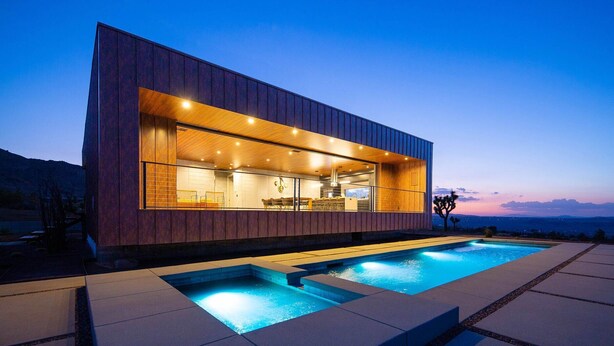Une maison moderne dotée d’une grande baie vitrée, d’une piscine et offrant une vue sur les montagnes.