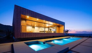 Une maison moderne dotée d’une grande baie vitrée, d’une piscine et offrant une vue sur les montagnes.