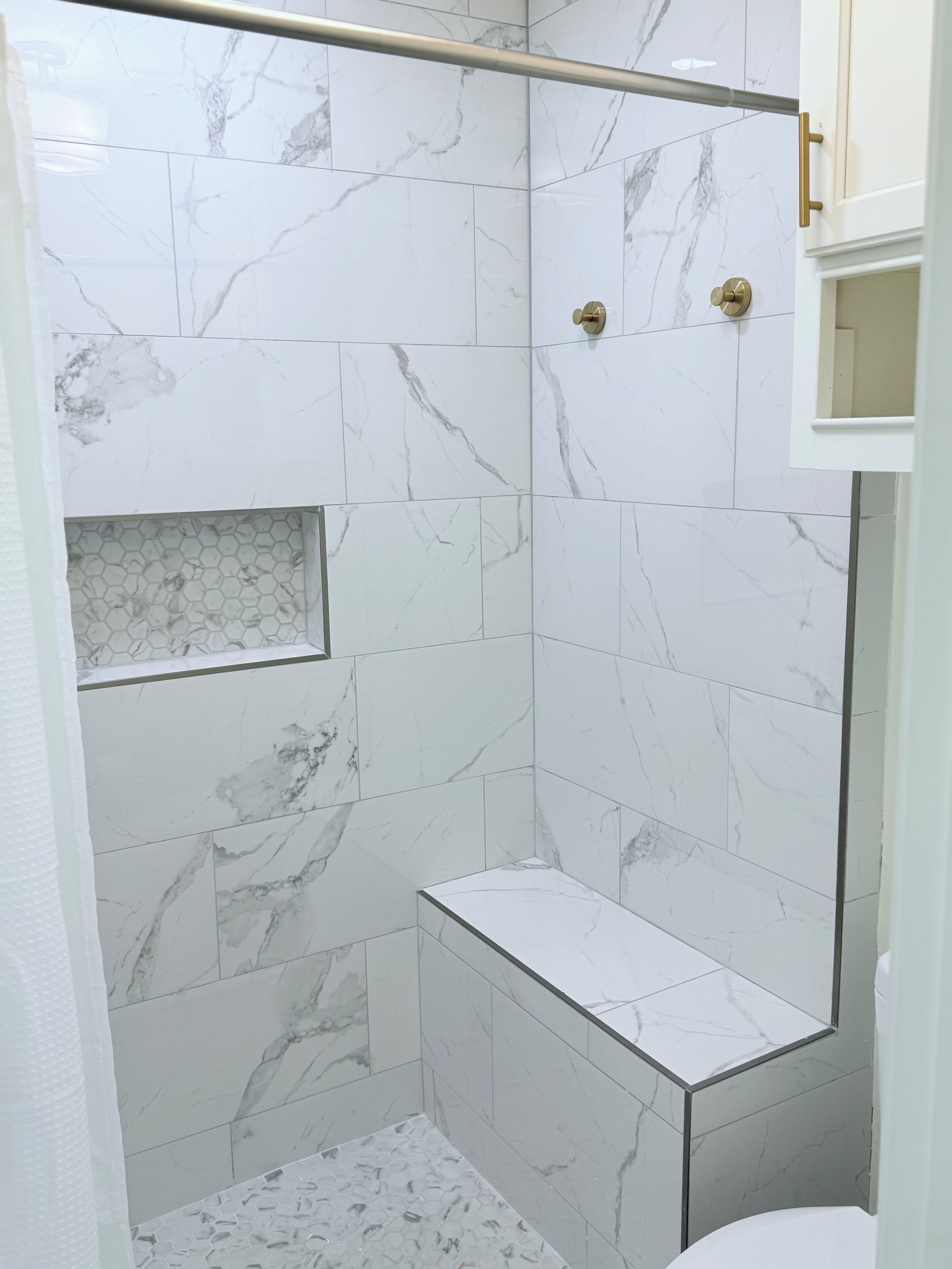Een douche met witte marmertegels en een douchecabine van glas.