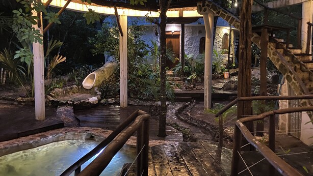 A wooden bridge over a small water feature, surrounded by greenery and a stone building in the background. - Tulum Jungle House with Swimming Pool - Relax and Spiritual Connection (Macario Gómez)