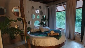 A circular bed with a wooden frame, surrounded by large windows and potted plants. - Tulum Jungle House with Swimming Pool - Relax and Spiritual Connection (Macario Gómez)