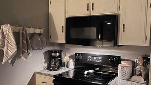 Une cuisine de taille réduite avec des meubles blancs, une cuisinière noire et un four à micro-ondes.